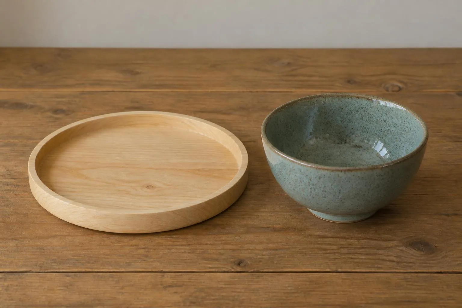 un plateau en bois brut et un bol en céramique émaillée posés côte à côte sur une table en bois