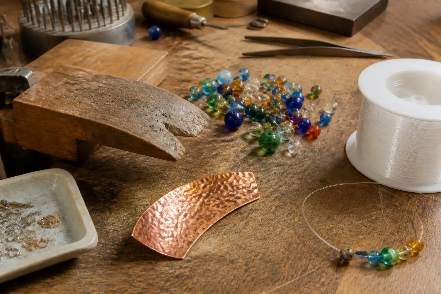 un établi de bijoutier avec des perles de verre colorées, un fil de nylon et un fragment de cuivre martelé